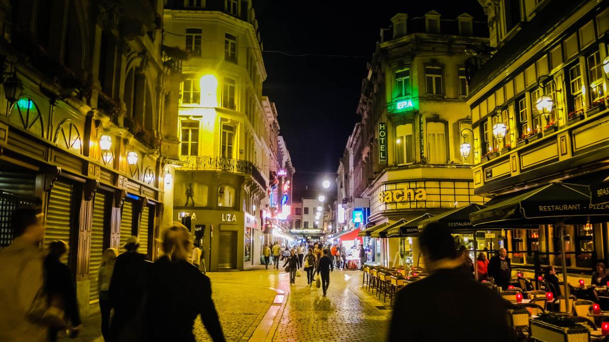 A lively Brussels street at night, lined with restaurants and warm lights
